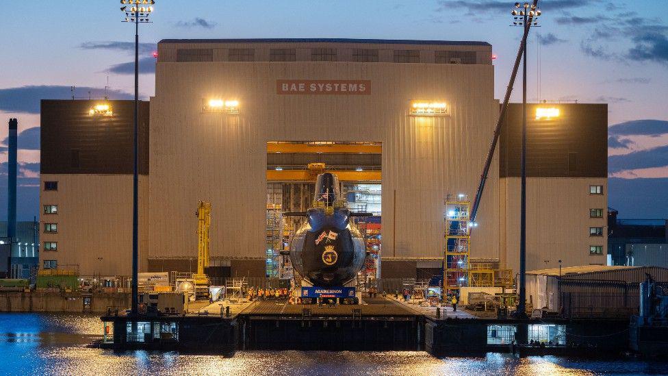 Front-on view of BAE hangar, a large white building, with HMS Agamemnon poking out of it.