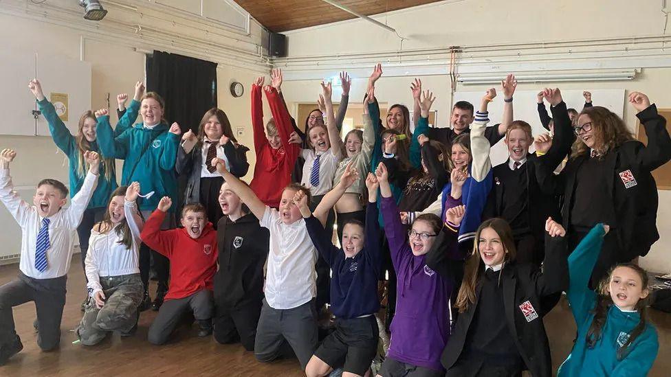 A group of children cheering with their arms raised at a youth club