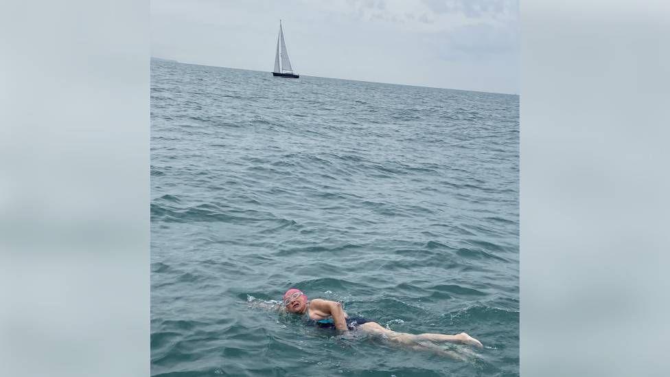 woman swimming in sea with boat in background