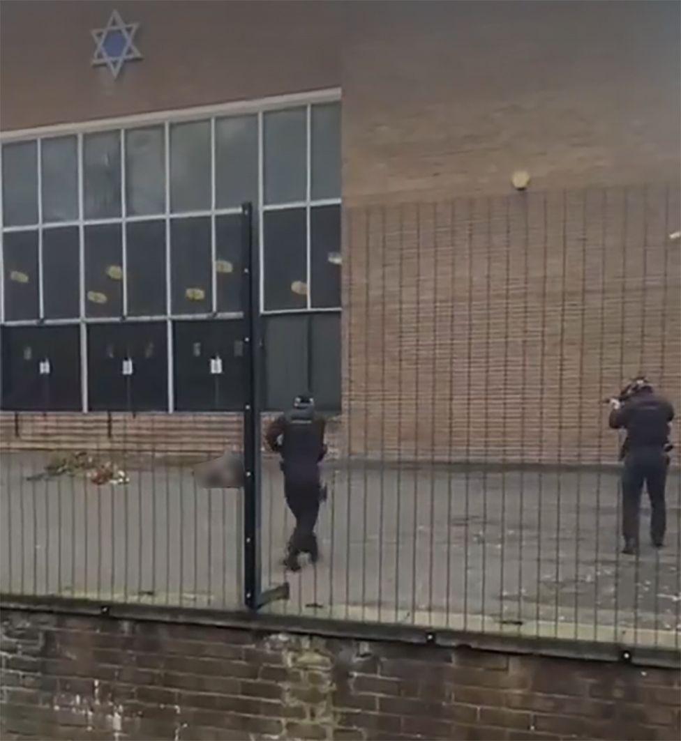 GMP firearms officers and the suspect, who has been shot, outside the synagogue in Manchester