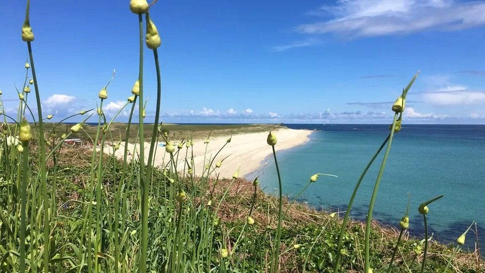 Shell Beach, a white sand beach on Herm Island in Guernsey. Blue sky with clouds and bright blue sea.