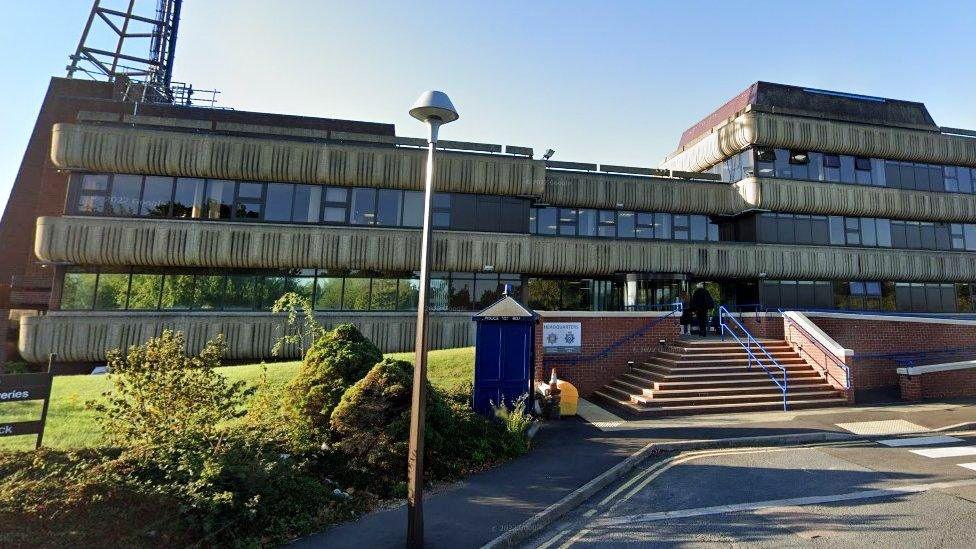 The exterior of Lincolnshire Police's headquarters. It is a two-storey concrete and glass building with red brick steps leading up to the front and an old blue police phone box at the front