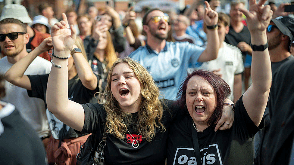 Fans in Oasis tee-shirts embrace and sing