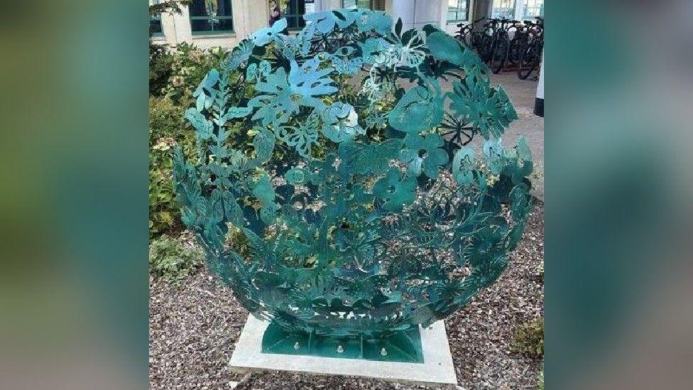 A close-up of the sculpture where it is possible to see in more detail the organ shapes, mixed with that looks to be nature elements like flowers, leaves and butterflies.