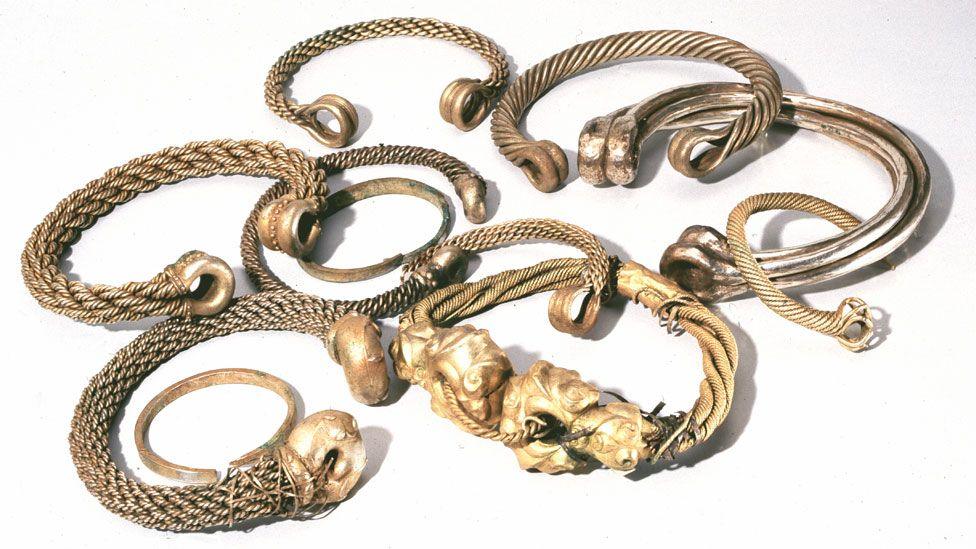 A range of Iron Age gold neck ring torcs lying on a white background. In between are two plain gold bracelet torcs.