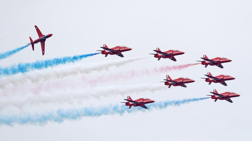 The Red Arrows at an air display. The red aircraft are trailing red, white and blue smoke