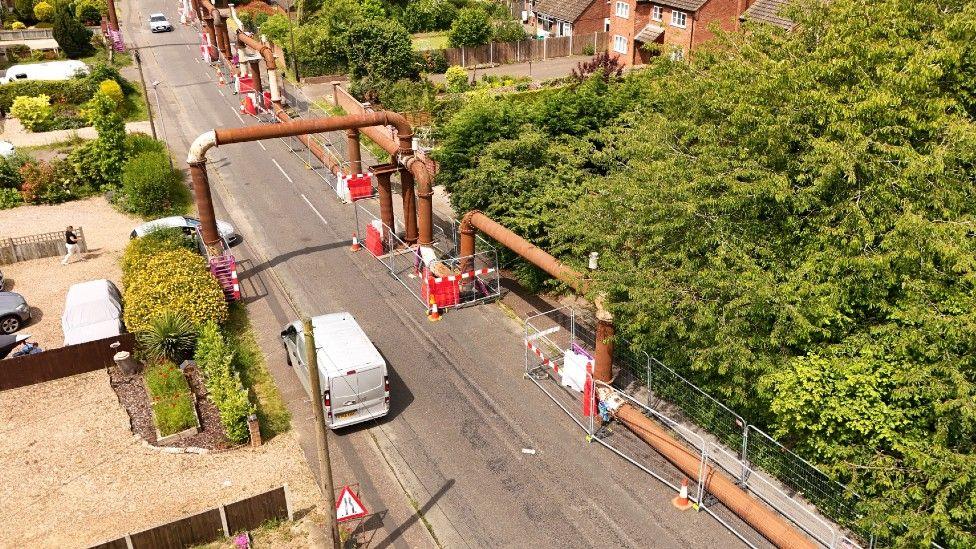 Aerial of sewage pipe in the road, passing houses and trees