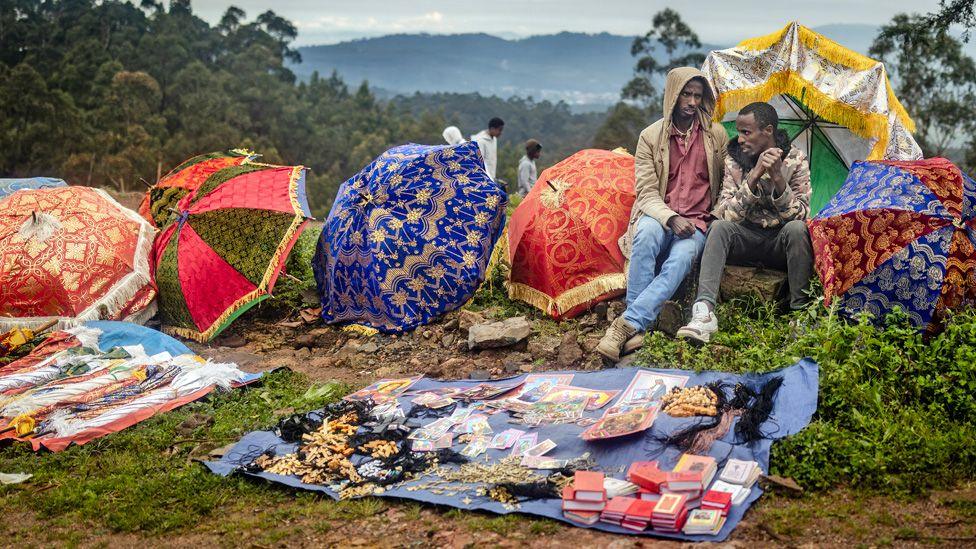 Two vendors wait for customers as they sell colourful ceremonial umbrellas and religious items on the roadside during a New Year church celebration at Entoto St Raguel Church in Addis Ababa, Ethiopia - Thursday 11 September 2025.