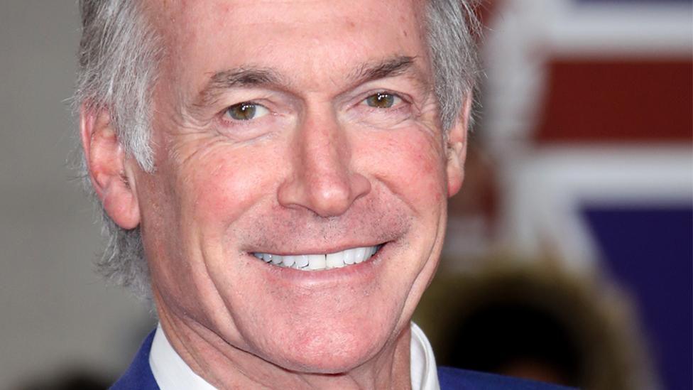 A close-up of a man with silver hair who is smiling at the camera.