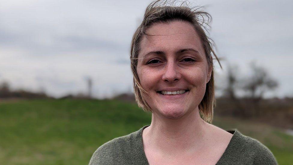 A woman looking towards the camera with her hair slightly blowing in a breeze, Stanwick Lakes