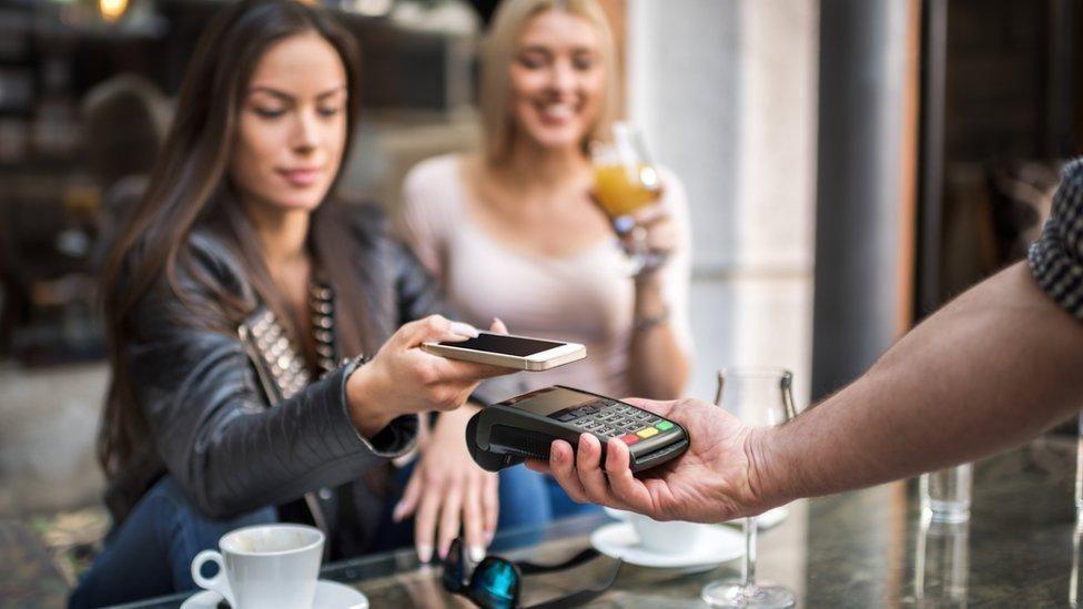 A woman in a leather jacket paying for her drinks by tapping a card machine with her phone