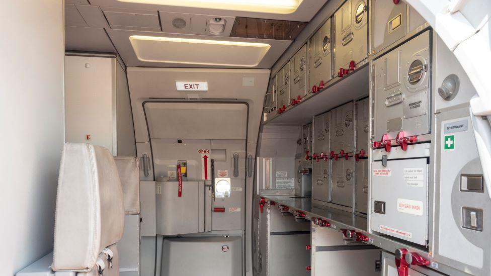 The galley on a plane with store cupboards and an emergency exit