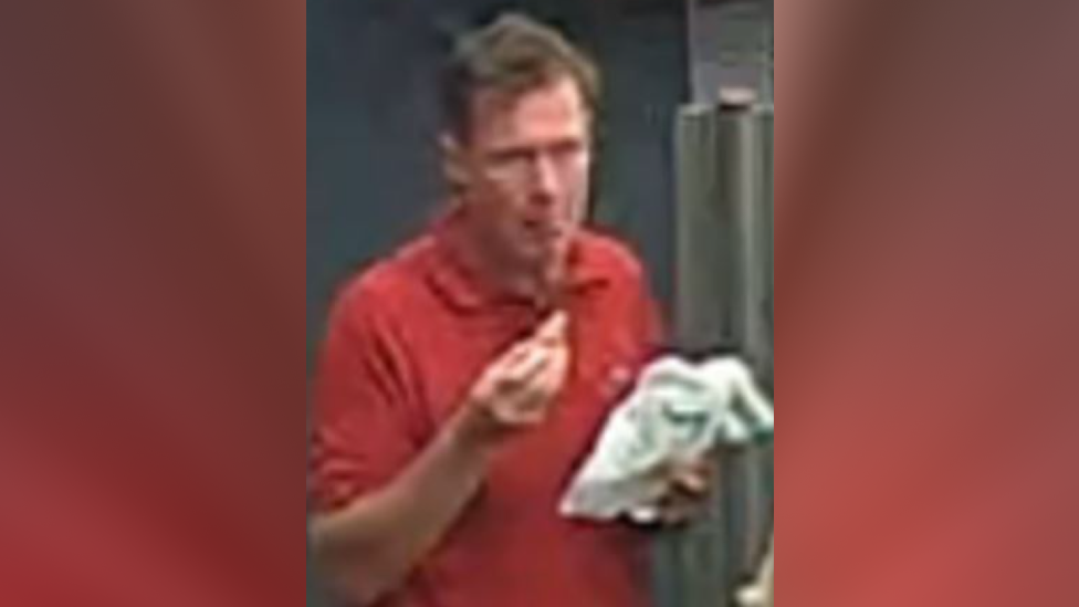 A blurry image of a man, with short brown hair, in a red T-shirt holding what appears to be a white bag