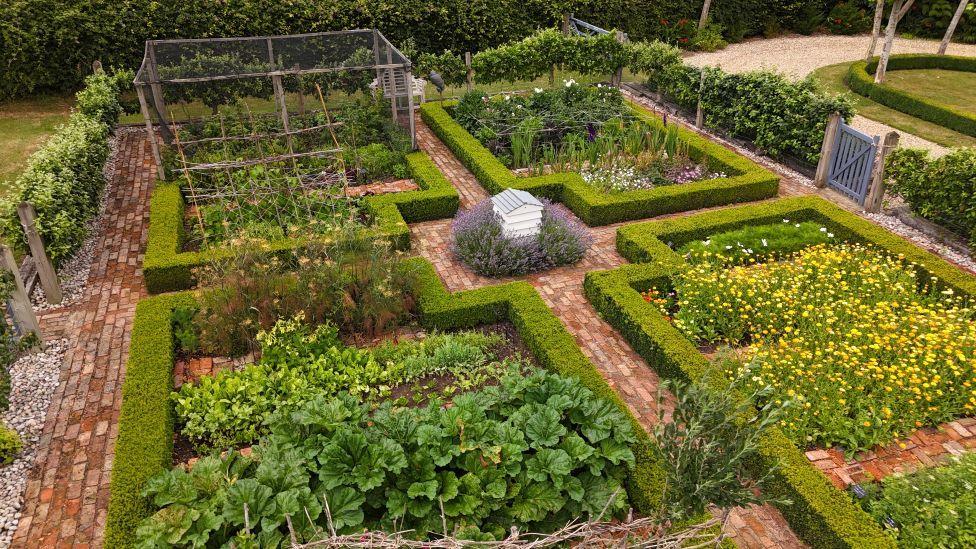 Part of the garden which shows hedges sectioning off vegetable patches and wild flowers. 