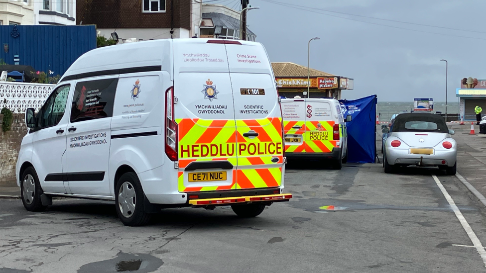 The end of Mackworth Road, leading to the beach and the sea at the end.
There is a silver car parked with police vans beside it. A restaurant can be seen in the background.