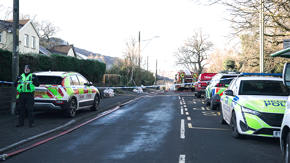 A police cordon has been put across a residential road, with emergency services vehicles parked at the scene