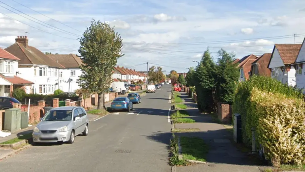 A Google street view screenshot of a sunny street with semi-detached houses on each side and cars parked on the roadside.