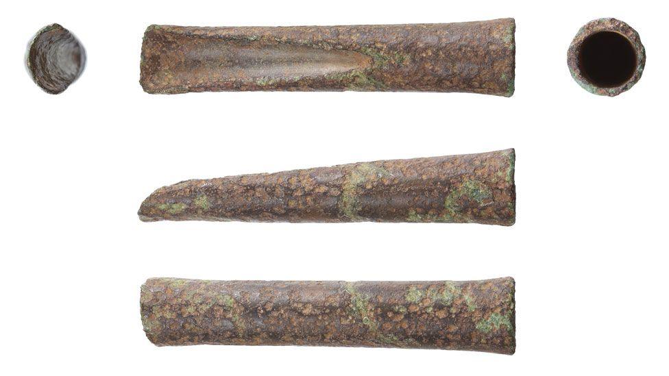 Five views of a bronze woodworking gouge against a white background. From the top there are three views. On left the cutting edge from above; middle the shaft from above showing the cast gouge running from its cutting edge on the left up towards its middle; the shaft from above showing its socket cavity. In the middle the tool from the side tapering towards the cutting edge on the left to the socket on the right. The bottom view shows the tool from behind with its cutting edge on the left and its socket on the right.