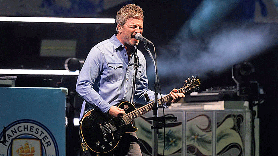 Noel Gallagher sings solo holding a black coloured guitar