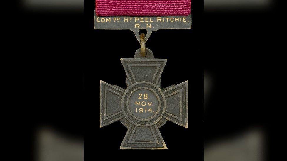 A cross-shaped medal with an inscription reading 'Comdr HY Peel Ritchie, 28 Nov 1914'