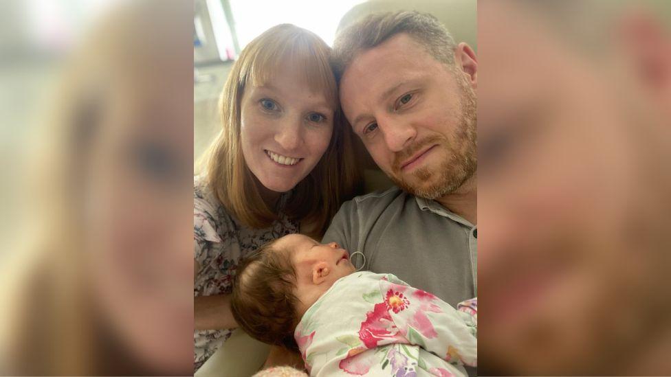 Pete Grimwade and his wife, Charlotte with baby Isabella in Pete's arms, in a close up shot