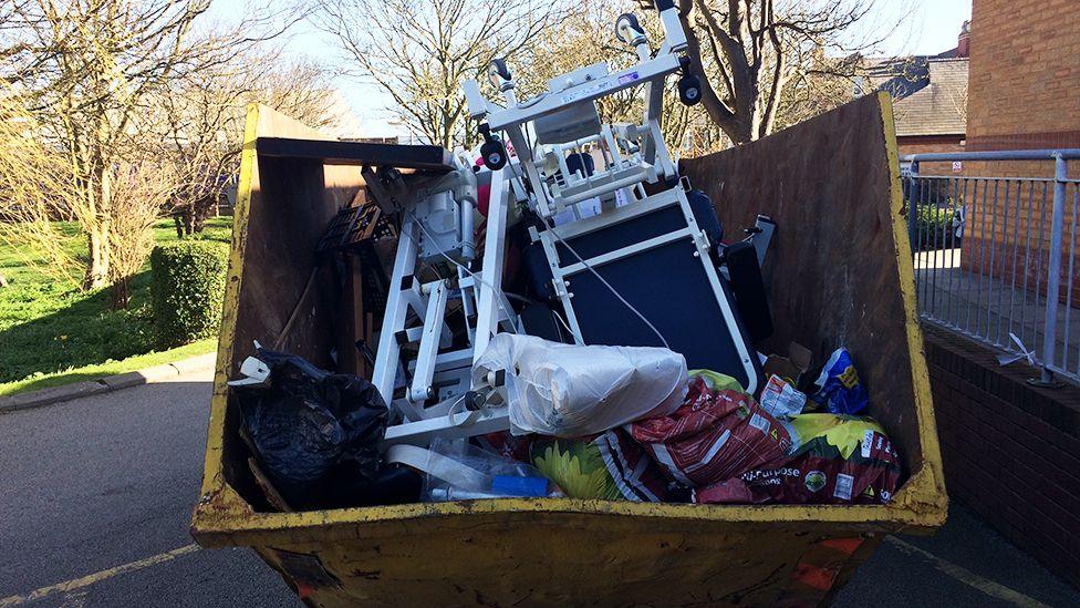 A yellow skip filled with furniture and other waste.