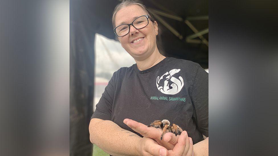 Sally Copson-Moore with brown hair and wearing black glasses and a black t-shirt from the Wirral Animal Samaritans holding a tarantula in her hands.
