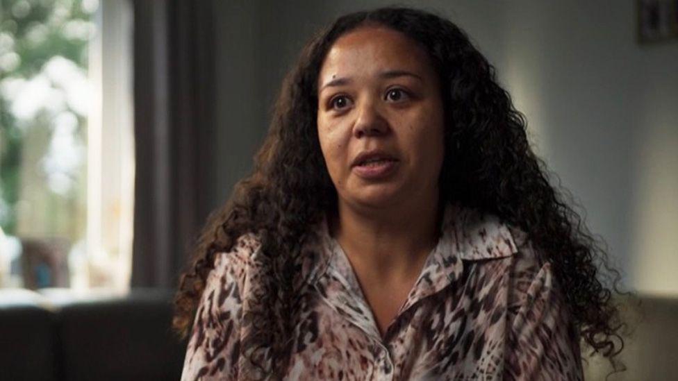 Jessica Cox, with dark curly hair and a leopard-skin top, speaking to an interviewer who is off camera. She is looking tearful.