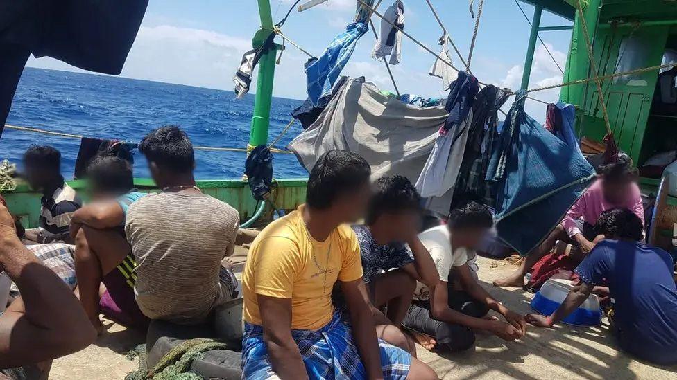 The Tamil migrants, with their faces blurred or turned away from the camera, sitting on the deck of a boat, with washing on lines around them, as they sailed through the Indian Ocean