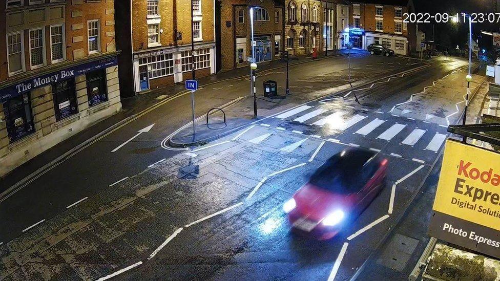 A CCTV image of a red car travelling southbound through a market town High Street