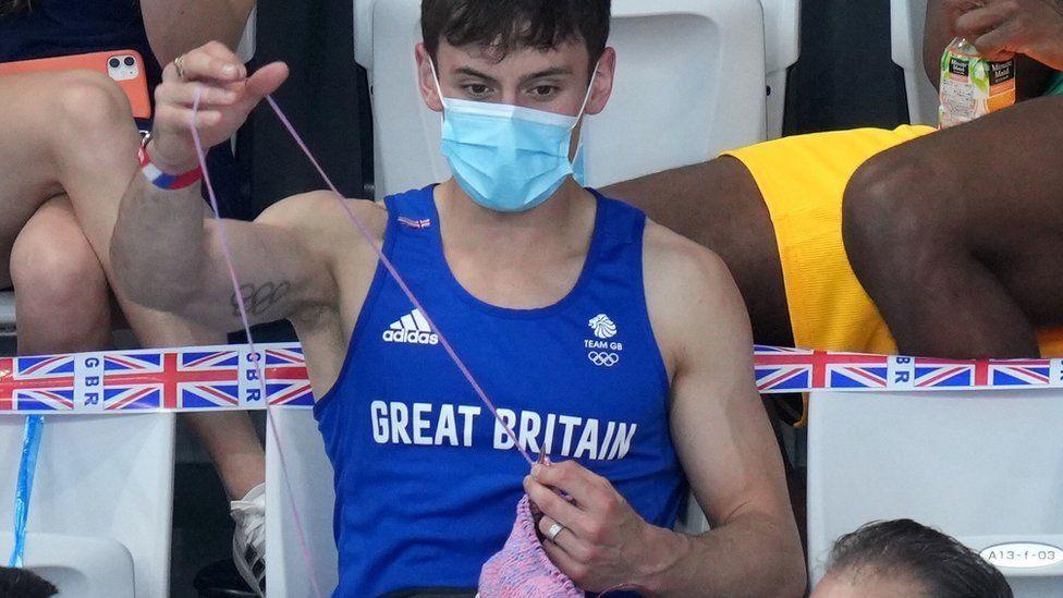 Tom Daley knitting while sitting in the stands at the Tokyo Olympics in 2021