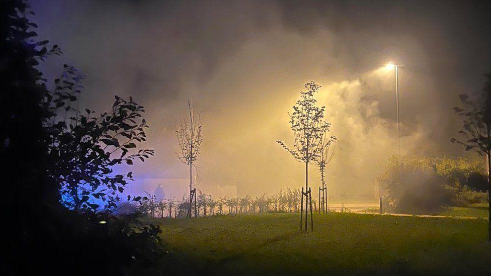 Smoke on grass with three small trees at night with a street light