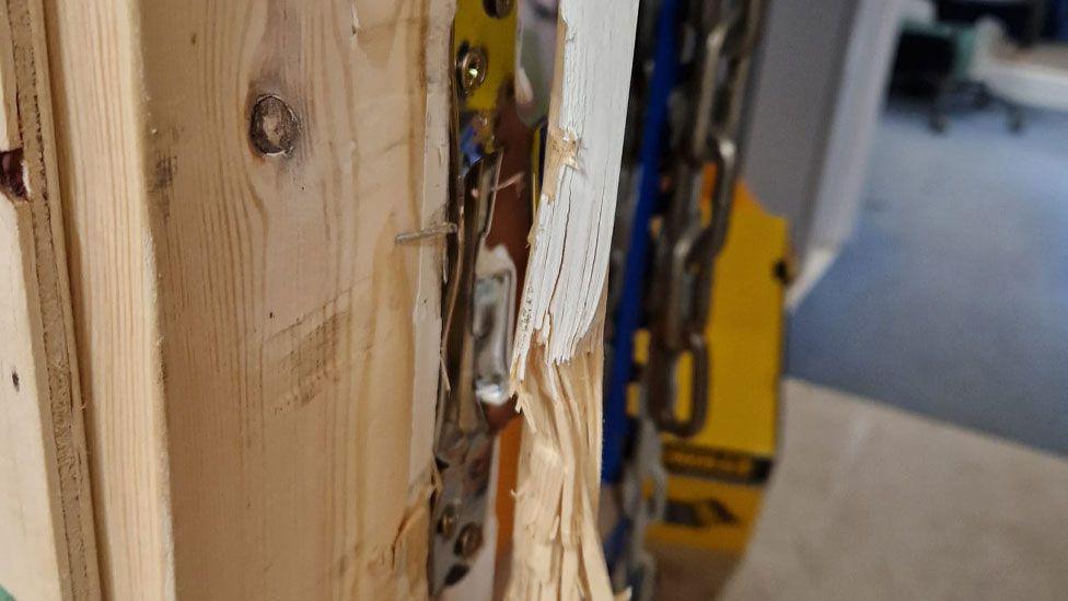 Close-up of splintered doorway with broken hinges at Emmaus Cambridge