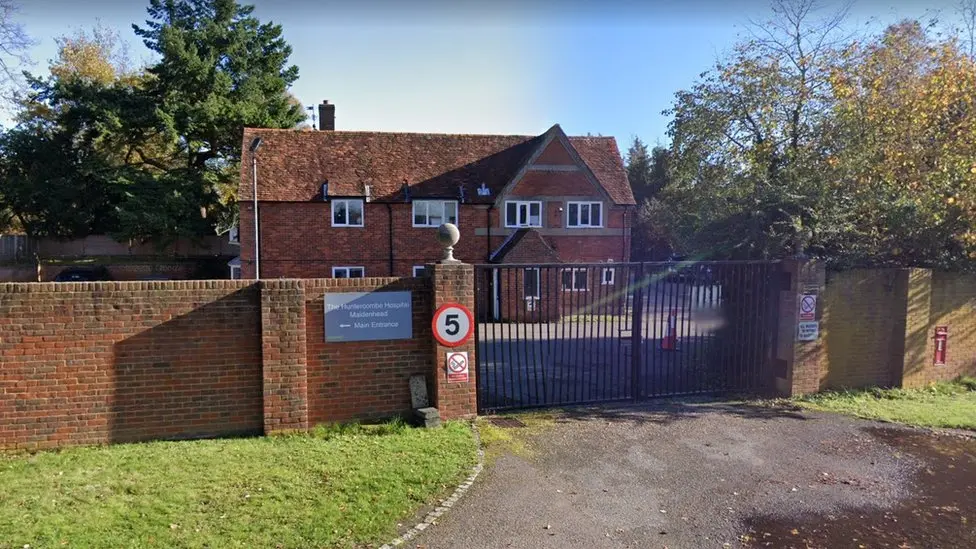 A Google Maps picture of Huntercombe Hospital, which is pictured behind black gates. It is a two-storey building. There is a 5mph sign on the left of the entrance.