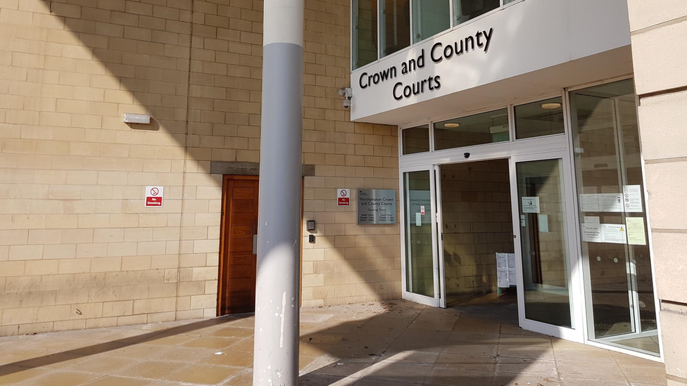 A courtyard before the entrance of Northampton Crown Court, with a sign reading "Crown and County Courts" above glass doors