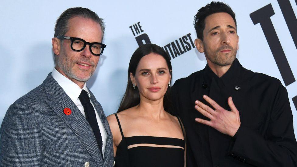 Guy Pearce, Felicity Jones and Adrien Brody pose on the red carpet at The Brutalist Los Angeles premiere in December.