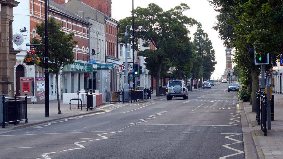 Cars driving along Lumley Road in Skegness towards a clock tower. The road is lined with trees on either side and a HSBC bank is on the left.