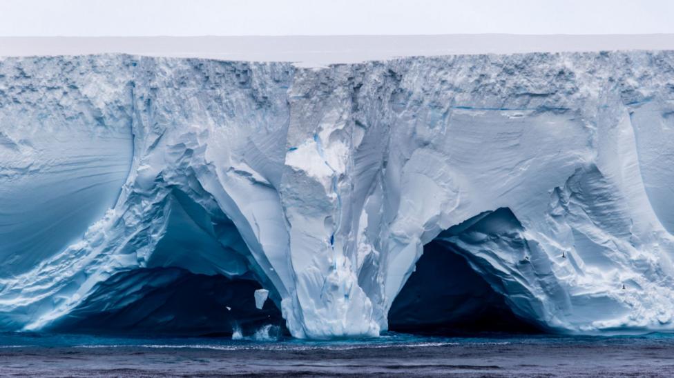 View of flat-topped ice cliffs with caverns cut into its side at sea level