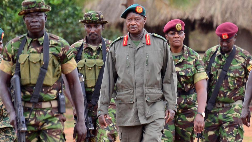 President Yoweri Museveni, in a green beret and khaki uniform, surrounded by members of the Special Forces Command (SFC) in green camouflage fatigues. Two are wearing maroon berets and two in floppy hats are armed with automatic rifles.