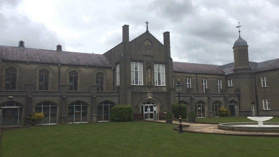 The St David's Building, known as the old building, at the Lampeter Campus. It is grey with a lawn, path and water feature, in front of it