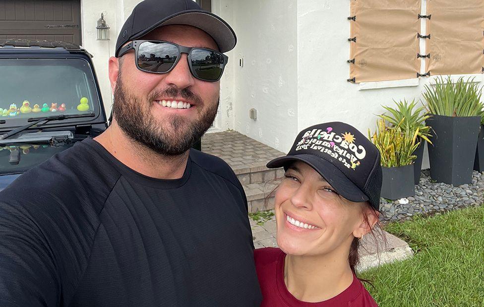 Sterling and Chynna Perkins, both wearing black caps, stand in front of a house