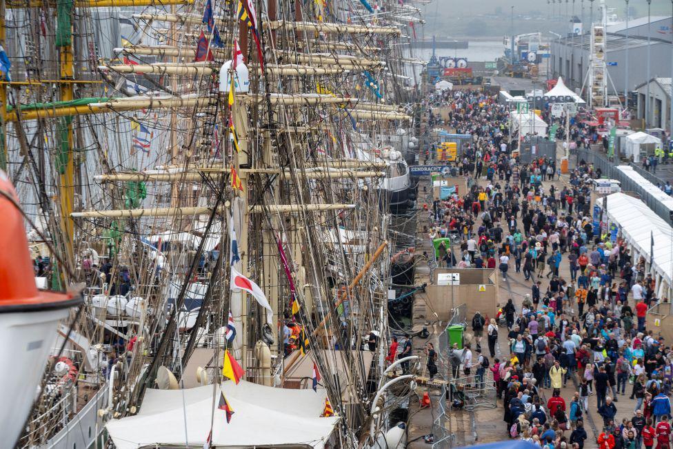 Hundreds of people on quayside next to tall ships at Aberdeen harbour.