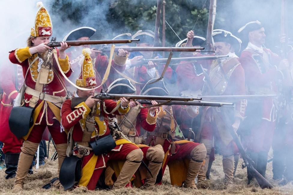 Re-enactment featuring people in 1745-style uniforms, amid gunsmoke