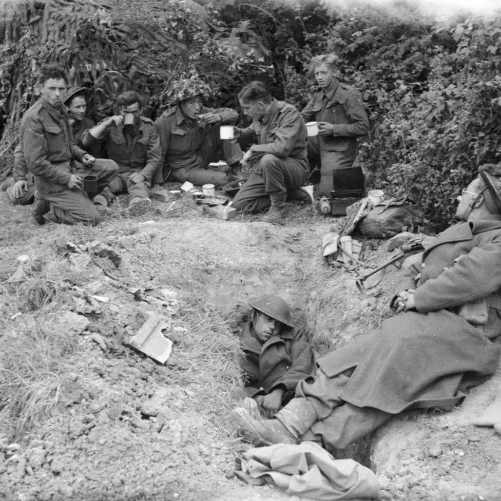 Black and white image of soldiers, some holding mugs.