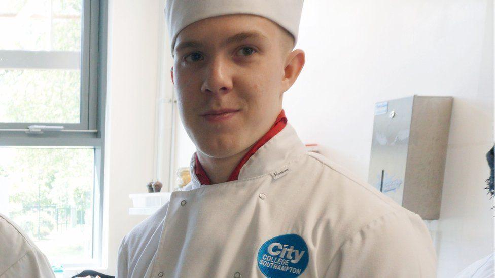 Joe Abbess is wearing a white chef overalls as he smiles into the camera