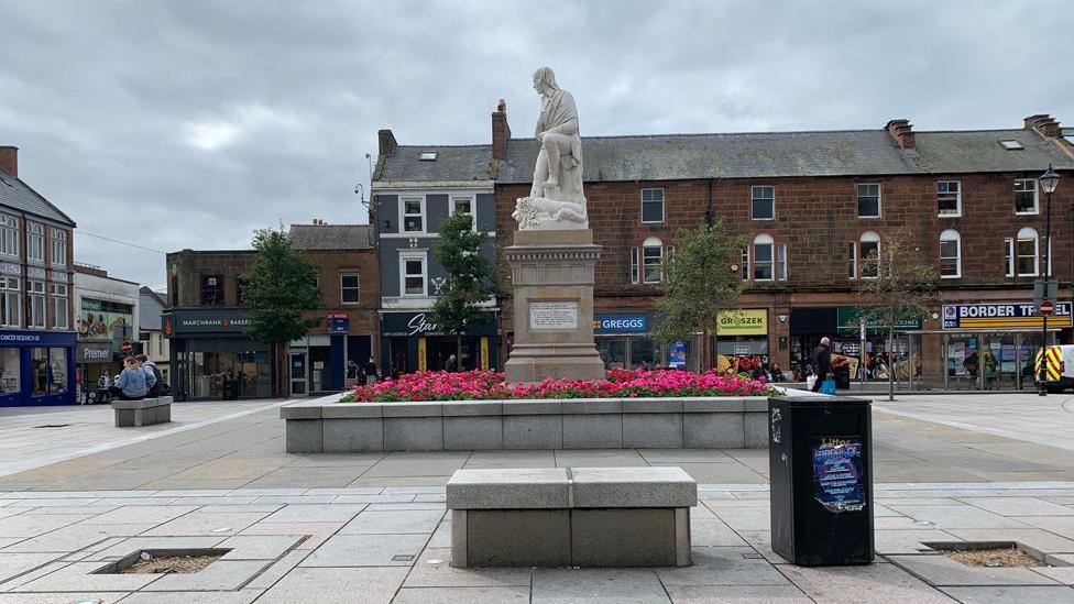 Burns Statue in Dumfries on a grey day with a row of sandstone shop buildings behind it