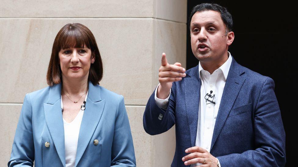 Rachel Reeves, with dark hair and a blue suit, stands next to Anas Sarwar, with dark hair and a dark blue suit