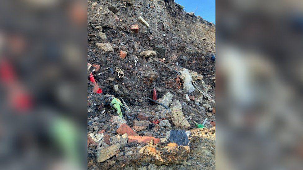 Several items made of plastic and other rubbish embedded in the cliffside.