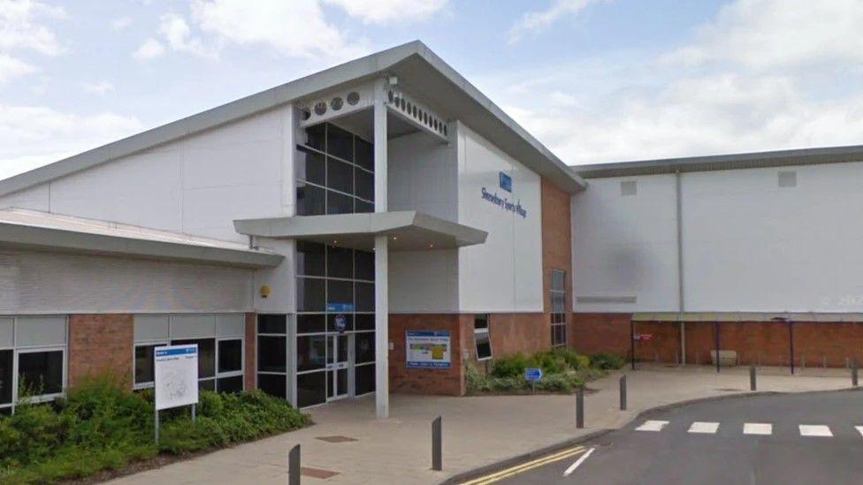 The outside of a leisure centre, which is white with red bricks and a glass front. A sign on the front says "sundorne sports village"