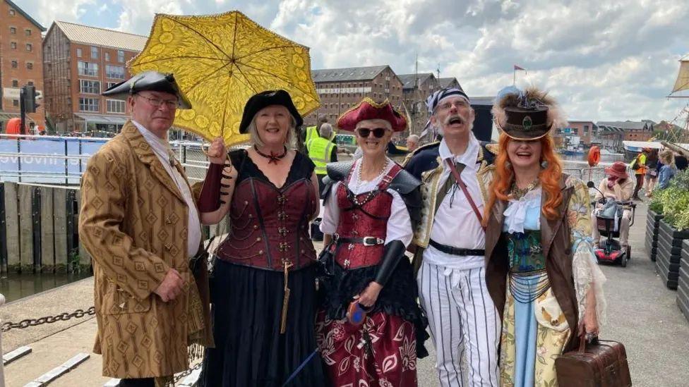 A group of five at the Tall Ships Festival 2024. There are two men and three women. They are all dressed up as pirates and smiling at the camera. 